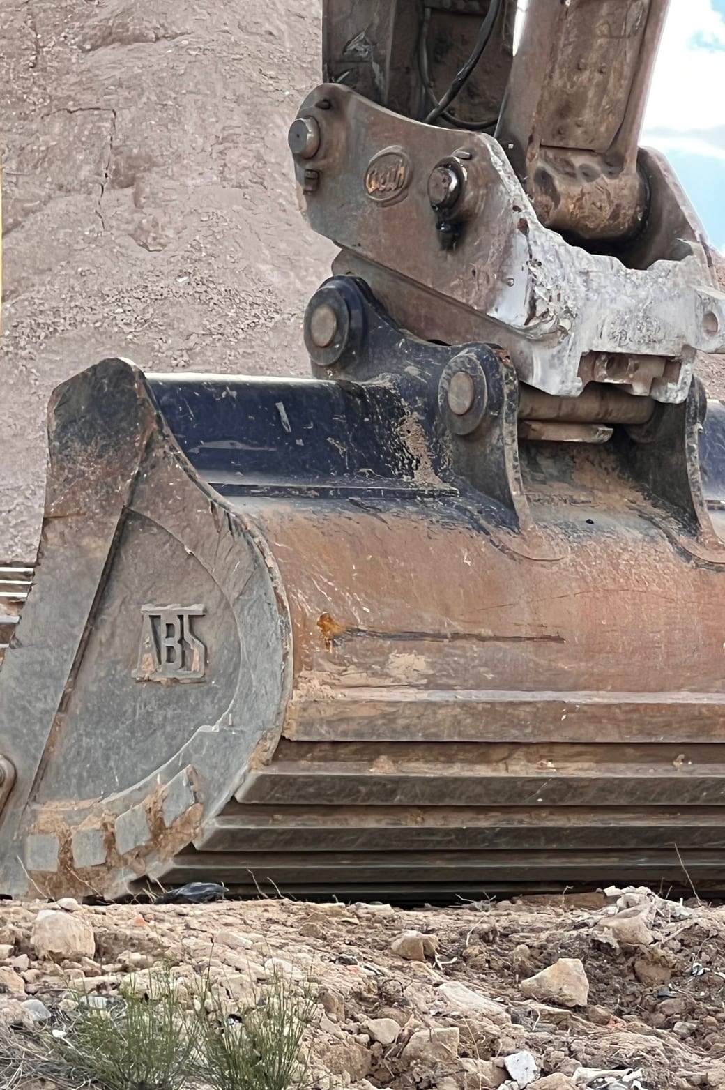 The bucket and quick-hitch of an excavator at close range at Glenfield Waste Services, worn steel against a stockpile.